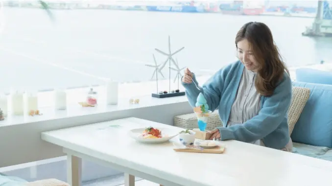 港を眺めながらカフェでスイーツを楽しむ女性